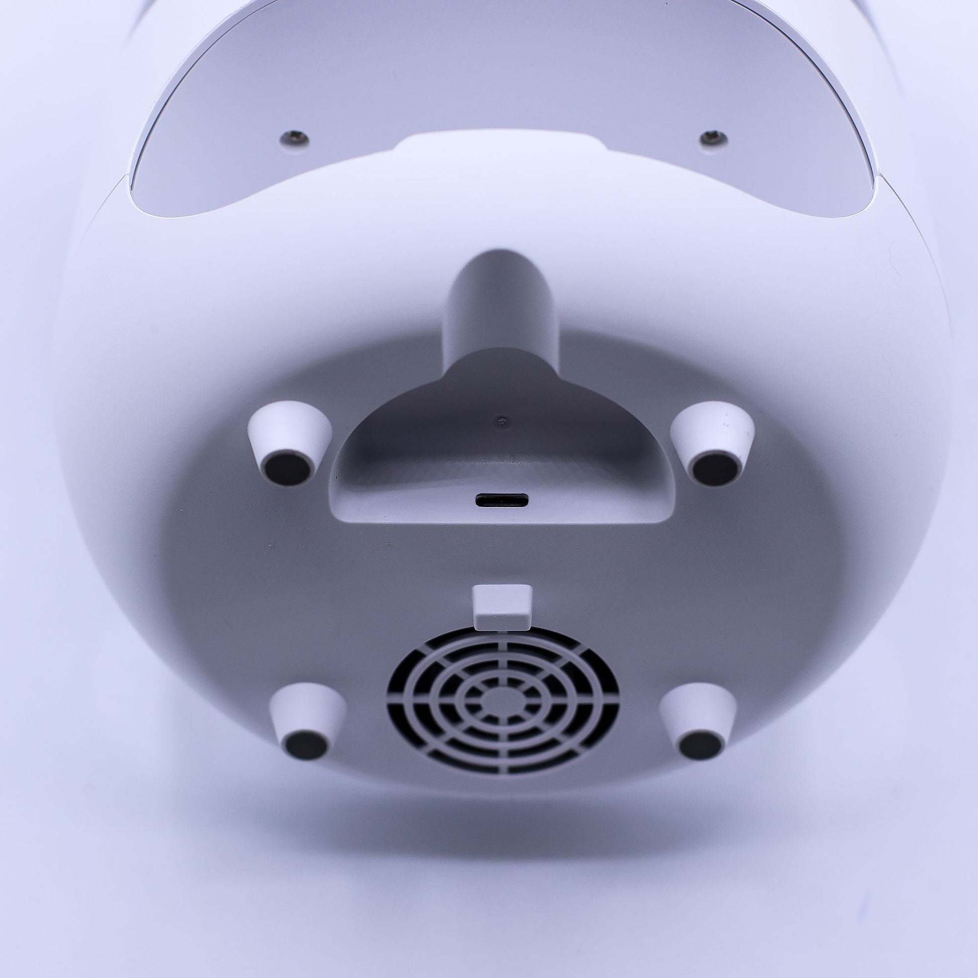 White cylindrical device resting upside down, exposing four conical rubber feet, a central USB-C port and curved handle, a circular ventilation grille, photographed against a plain white background.