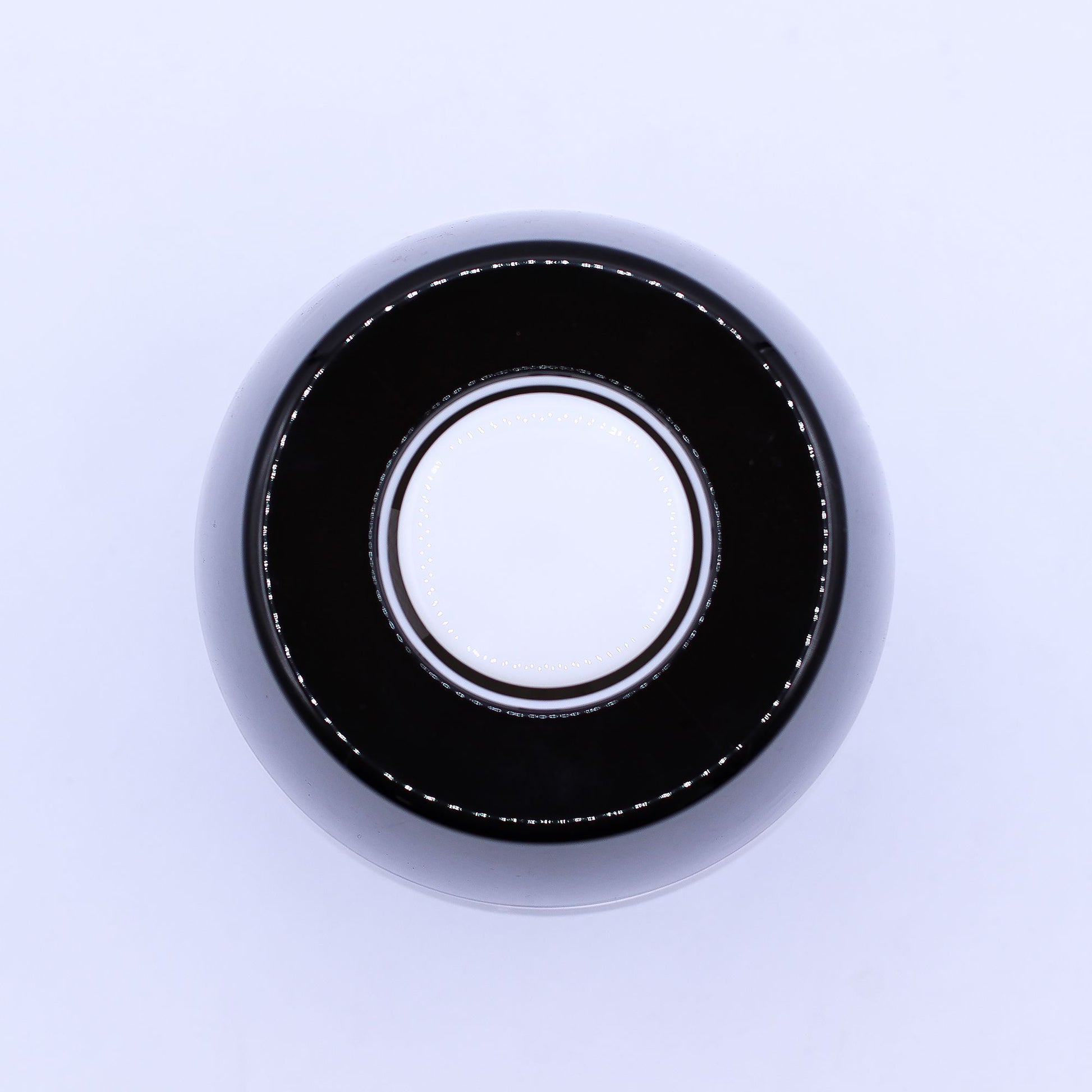 Glossy black circular ring surrounds a white concentric disk, reflecting tiny LED-like points, viewed from above on a pale, evenly lit background.