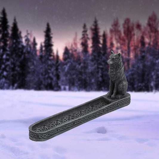 Stone wolf figurine sits at one end of a carved incense tray against a snowy forest at dusk.