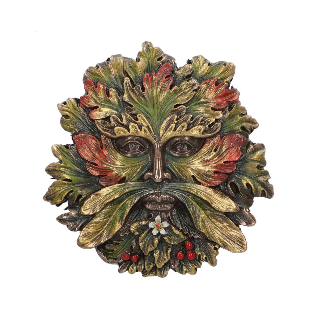 A sculpted face composed of leaves in autumnal colors, red berries, and a white flower forms a mask-like design. The intricate foliage surrounds the face, creating a natural, mystical appearance.
