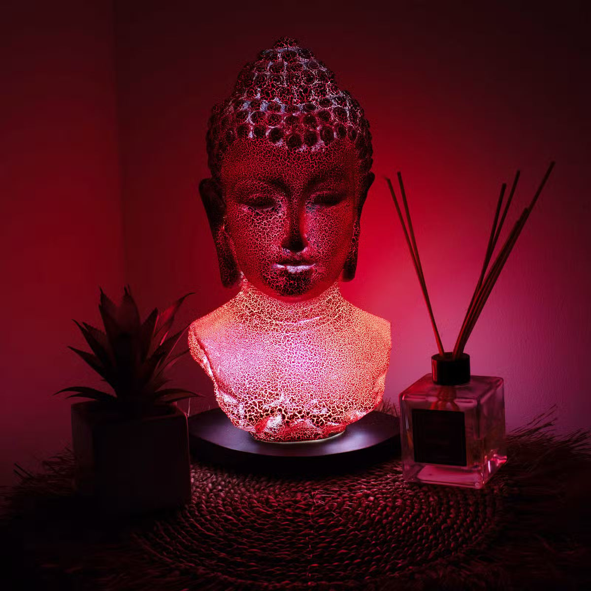 Molten Lava Buddha bust lamp with warm orange-red crackle glow and black oval stand UK