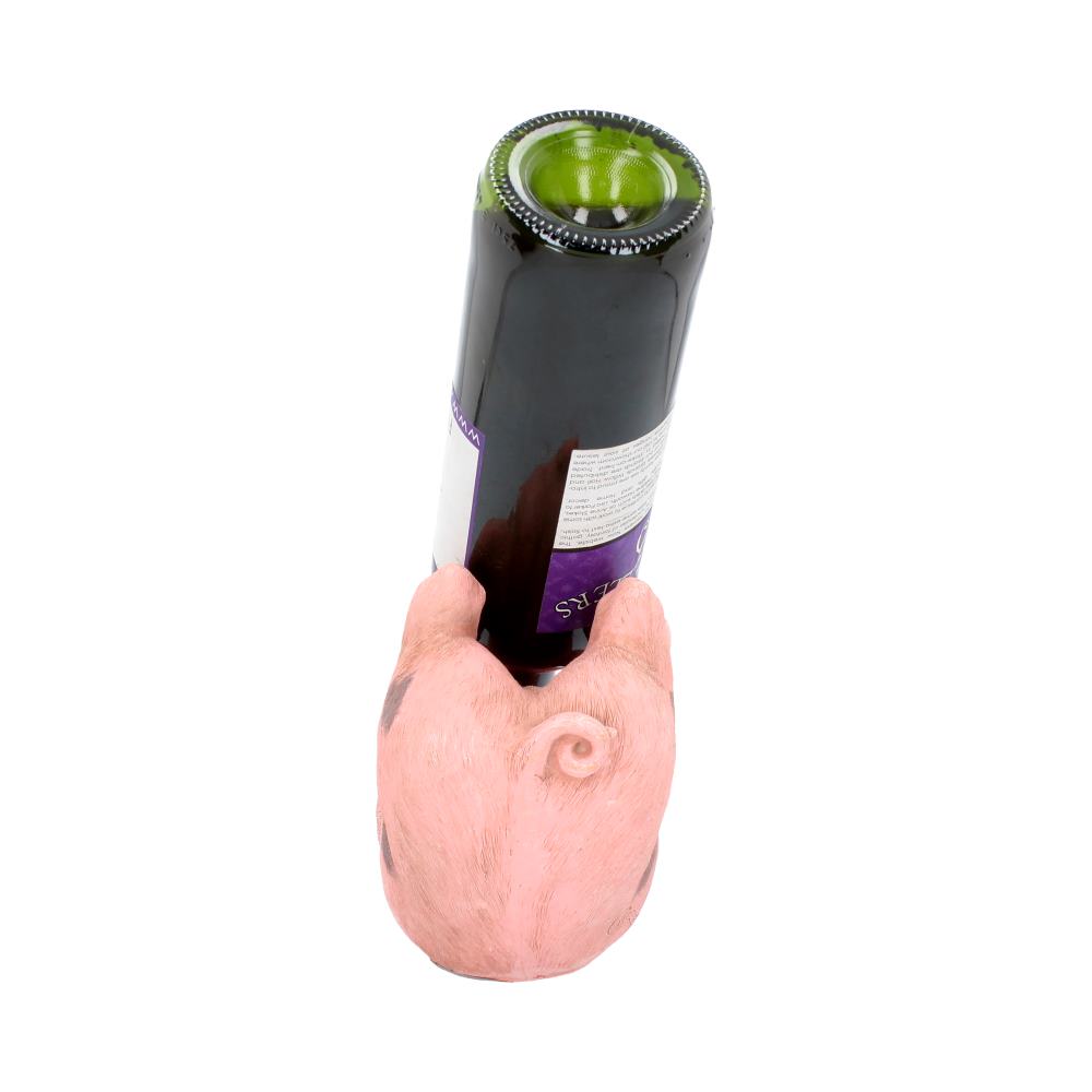 A wine bottle rests in a pig-shaped holder, positioned upright with the pig's back visible. The setting is a plain, white background. No text is visible.