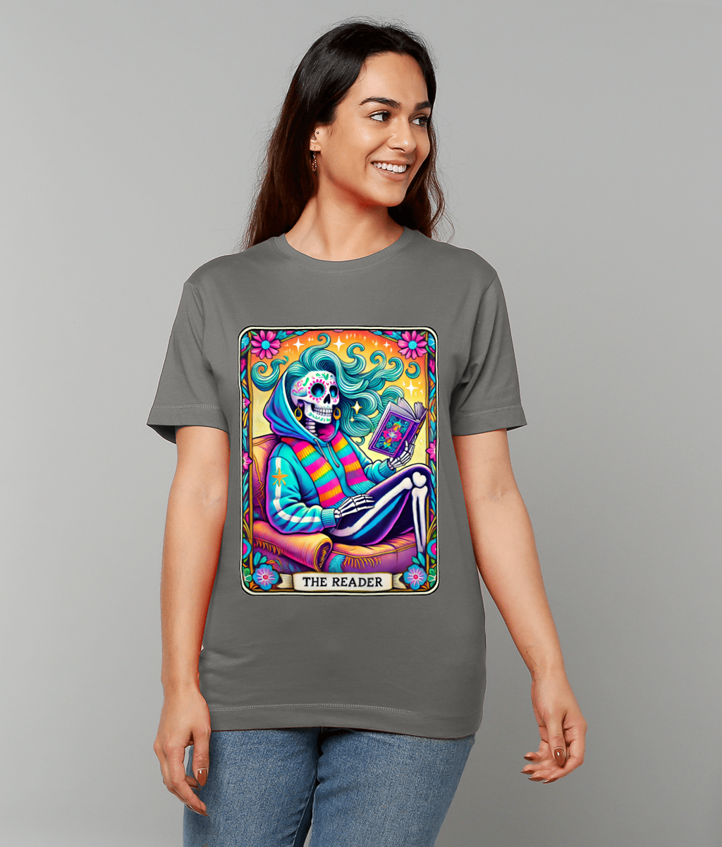 Colorful skeletal figure reading a book while seated in an armchair, wearing a striped scarf with flowing hair and a floral border on a T-shirt; text on design: THE READER.