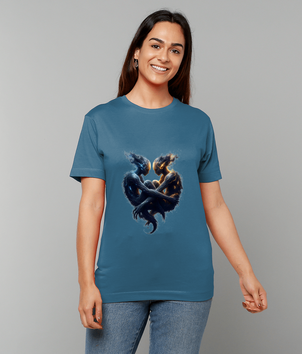 Smiling woman stands wearing a teal T-shirt printed with two intertwined fiery and watery humanoid figures forming a heart, hands relaxed at sides against a plain light gray studio background.