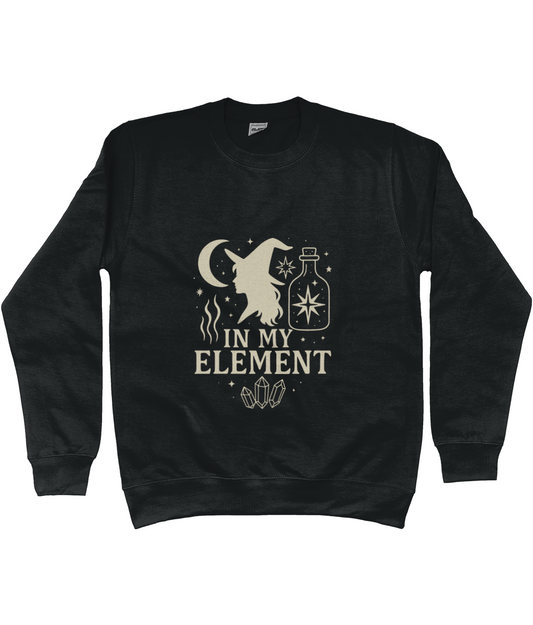 Black sweatshirt displays a beige witch silhouette, crescent moon, potion bottle, crystals and the text "IN MY ELEMENT" centered on a plain white background.