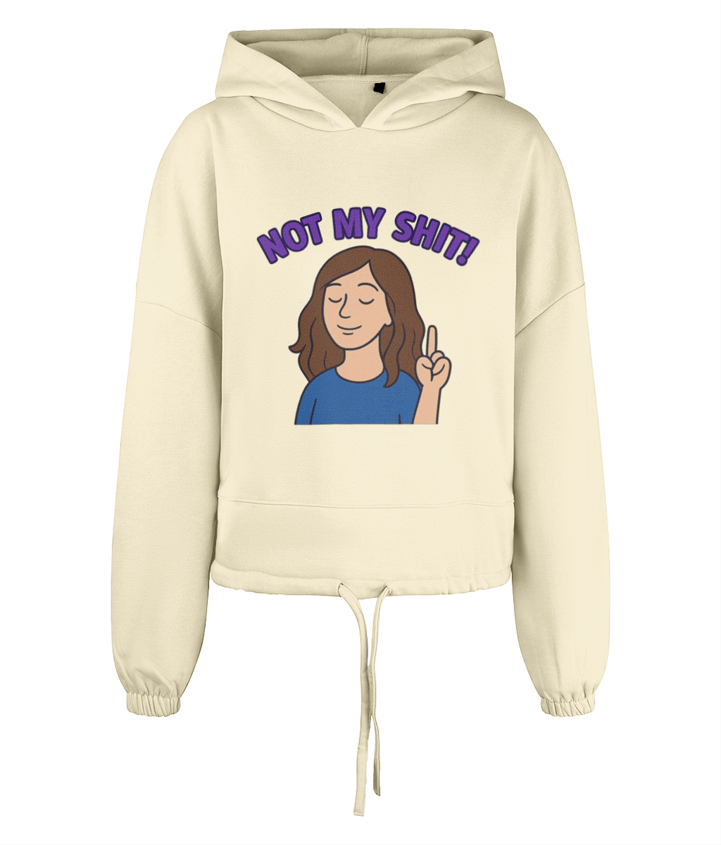 Cream cropped drawstring hoodie shows a cartoon woman with closed eyes raising two fingers while purple arched text reads 'NOT MY SHIT!' centered on the front against a black background.