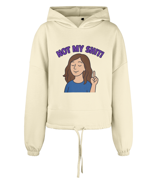 Cream cropped drawstring hoodie shows a cartoon woman with closed eyes raising two fingers while purple arched text reads 'NOT MY SHIT!' centered on the front against a black background.