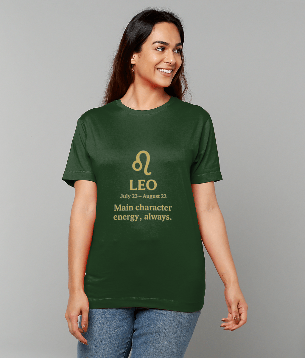 Woman wearing a green T-shirt printed "♌ LEO July 23 – August 22 Main character energy, always." smiling and looking to her right while standing against a plain light gray background.
