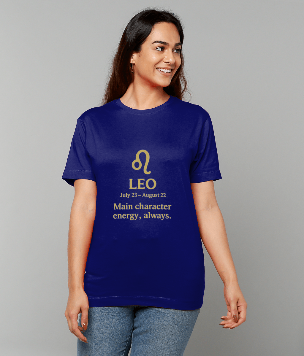 Woman wearing a royal blue T-shirt featuring a gold Leo symbol and the text "LEO July 23 – August 22 Main character energy, always." smiling and looking to the right against a plain light gray background.