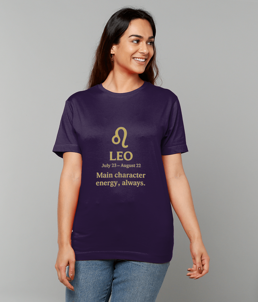 Purple T-shirt displays a gold Leo glyph and text "LEO July 23 - August 22 Main character energy, always." worn by a smiling person against a plain light-gray background