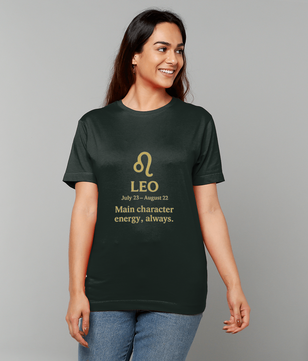 Woman wearing a dark green T-shirt, smiling and looking right against a plain gray backdrop; shirt displays the symbol and text: ♌ LEO July 23 – August 22 Main character energy, always.