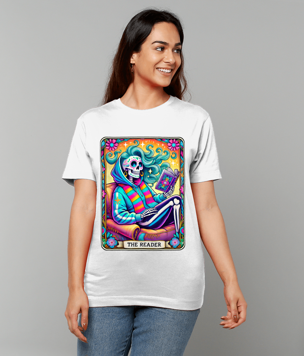 Colorful Day of the Dead skull character reads a book on a framed T-shirt graphic captioned "THE READER" worn by a smiling woman against a neutral studio background.