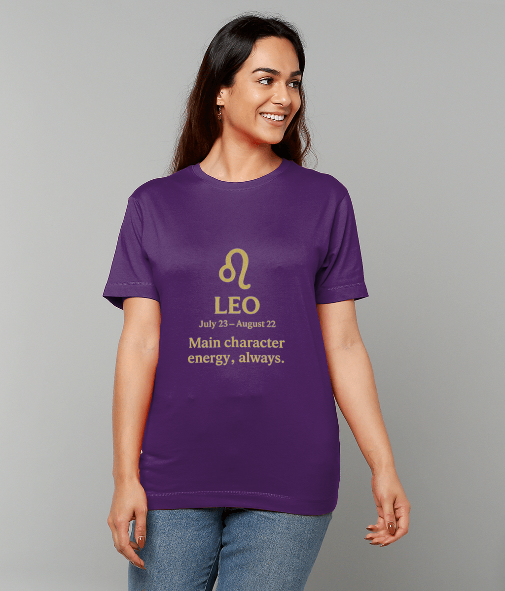 Woman wearing a purple T-shirt smiles while standing against a gray background; shirt displays a gold Leo symbol and the text "LEO July 23 – August 22 Main character energy, always."
