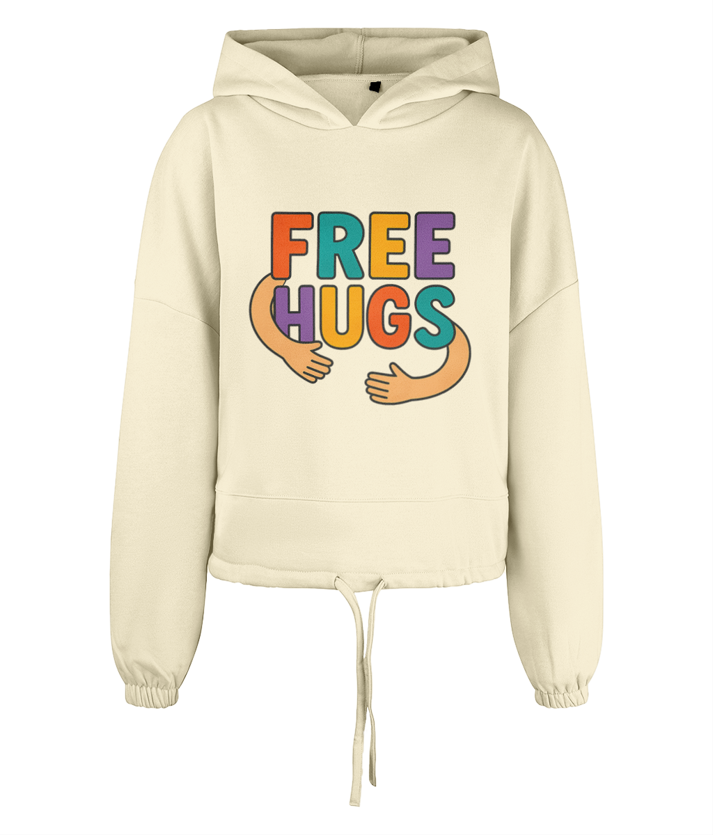 Cream cropped hoodie displays large colorful graphic reading "FREE HUGS" with cartoon arms forming a hug across the chest, shown centered against a plain black background.