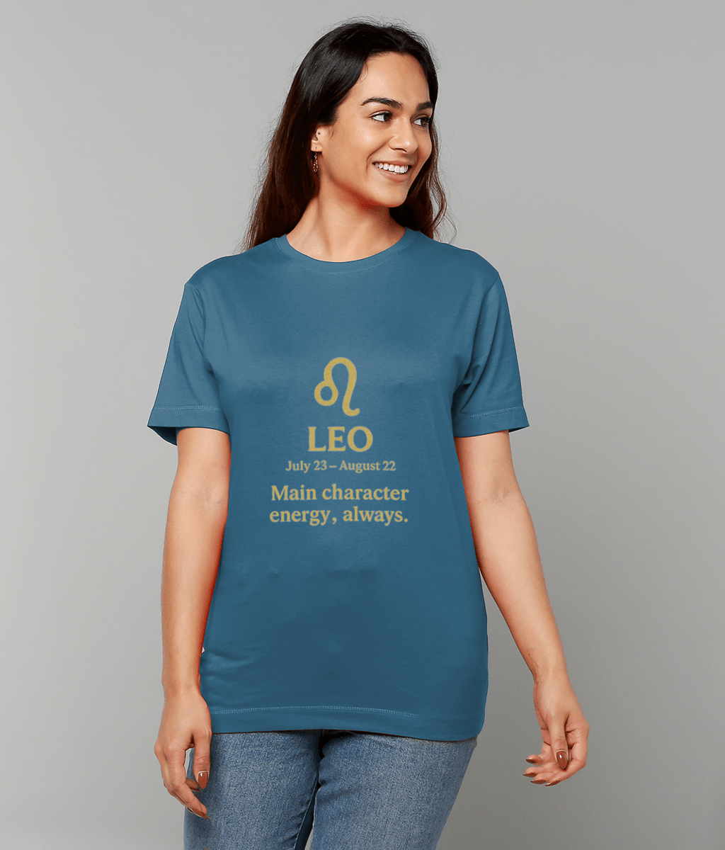 A woman wearing a teal T-shirt that displays the Leo glyph and text "LEO July 23 - August 22 Main character energy, always." is smiling and looking to the right against a plain light gray background.