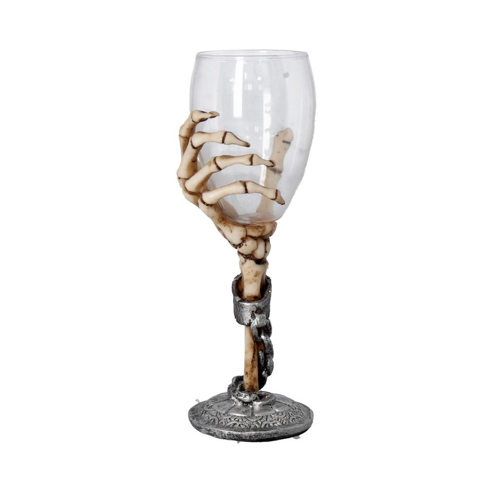 A wine glass is held by a skeletal hand that forms the stem, which is further decorated with silver rings and a hanging chain, placed against a plain, white background.