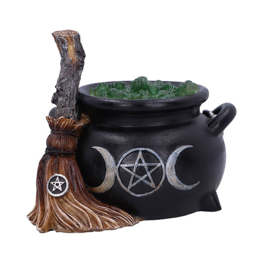 A black cauldron with a bubbling green potion displays a pentagram and crescent moons. A broomstick with a pentagram emblem rests beside it, suggesting a witchcraft theme.
