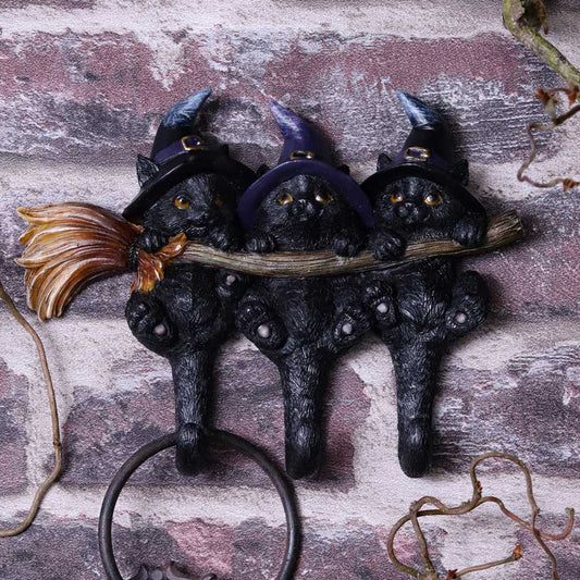 Witches Helpers key hanger by Nemesis Now with three black cats wearing purple witch hats, holding a broomstick with their tails forming key hooks