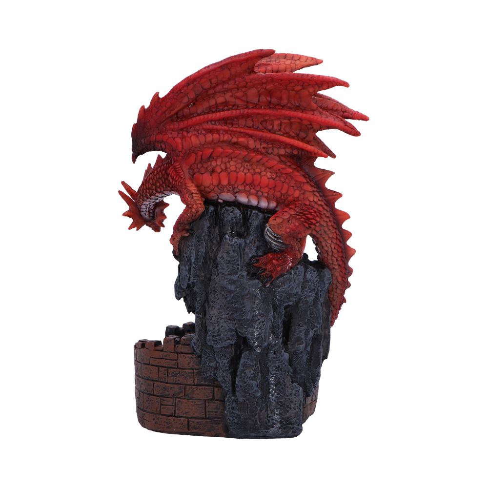 A red dragon figurine perches atop a dark, craggy rock formation, resembling a small, brick-walled structure; isolated on a white background.