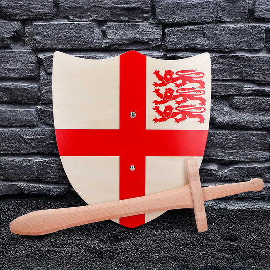 Wooden shield bearing a red St George cross and three red lions leans against a gray brick wall with a wooden sword resting across its base on a black floor.